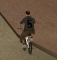 GTA 산 안드레아스에서 Base 5 로고가 박힌 티셔츠와 야구 모자를 착용하고 BMX를 타는 보행자.